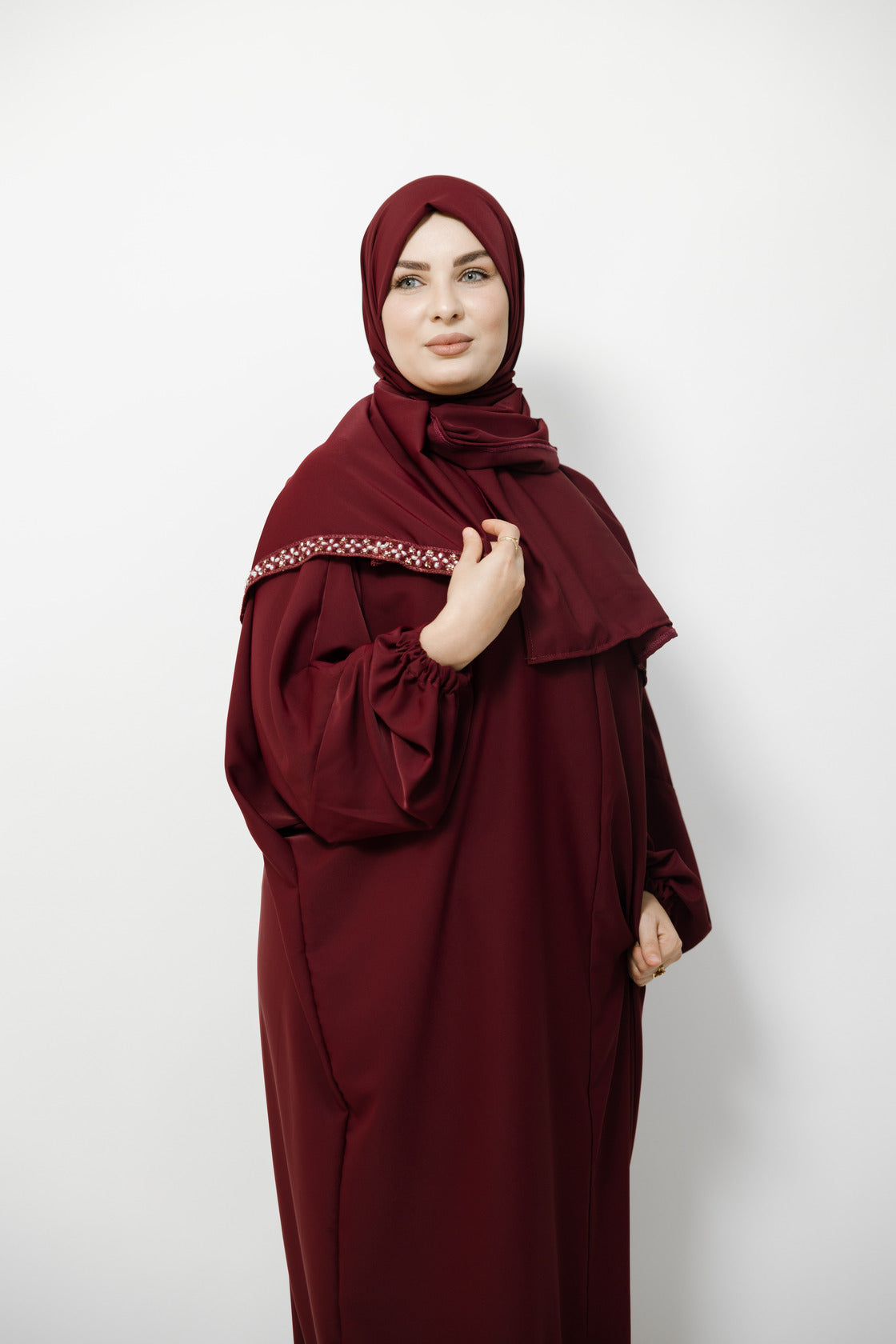 Woman wearing a burgundy abaya with a matching hijab on a white background