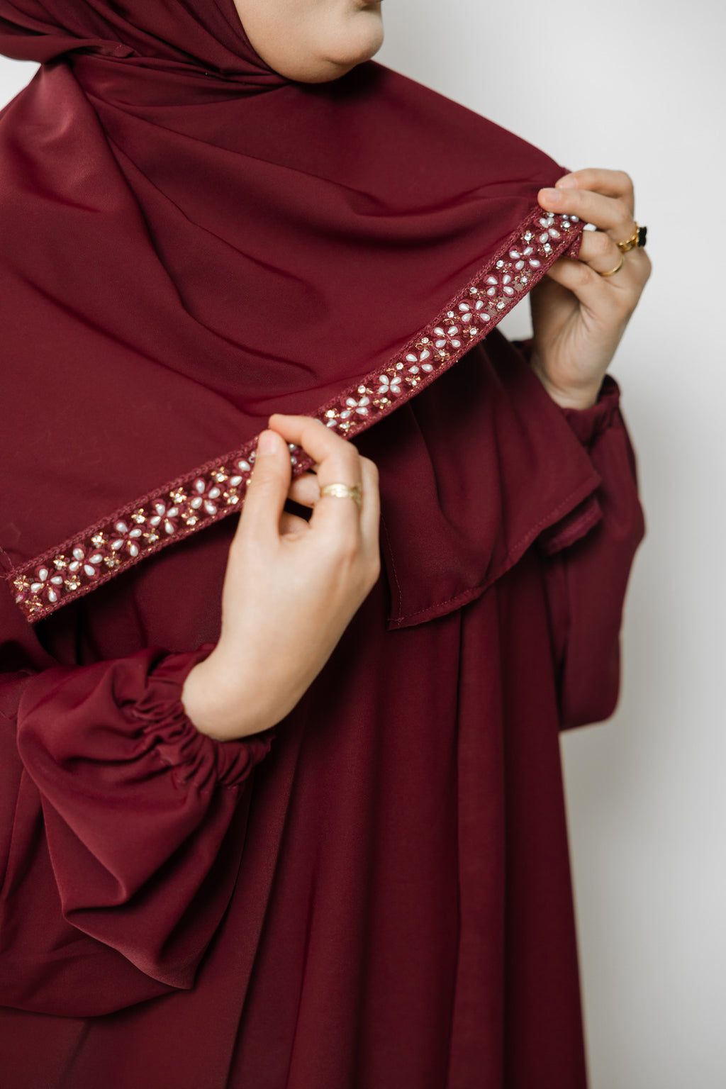 Maroon abaya with embellished hem against a white background