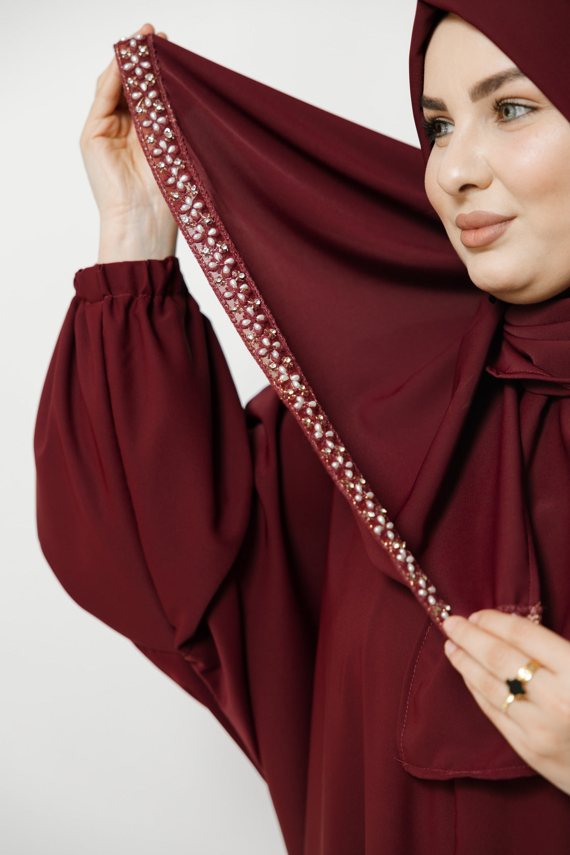 Woman wearing a burgundy abaya with intricate detailing on a white background